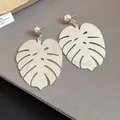 Primo piano di orecchini a foglia di monstera color argento con dettagli traforati su grigio - Argento