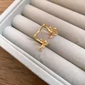 Detailed close-up of a gold bow ear cuff jewelry piece in a grey velvet tray. - Clip-On Earrings / Gold