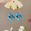 Close-up view of elegant blue enamel flower dangle earrings with golden stamens and edges. - Silver Earring Post-Blue