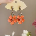 Close-up of sweet orange oil-drop flower earrings on a cloud-shaped display card. - Orange (Silver Needle)