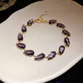Detailed macro view of an elegant purple teardrop zircon bracelet on white ceramic. - Gold-Purple