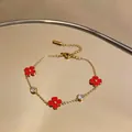 Vista detallada de una pulsera de acero dorado con flores rojas y dijes de circonita - Dorado-Rojo