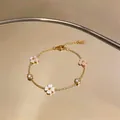 Primer plano detallado de una pulsera de acero inoxidable dorada con flores y circonitas - Oro-Blanco