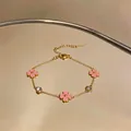Elegante pulsera de acero dorado con flores rosas y circonitas claras, vista de detalle. - Oro-Rosa