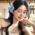 Close-up of a blue fabric flower hair clip worn by a model in a cozy cafe setting - Duckbill Clip (Single Piece) / Blue