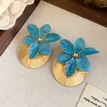 Detail shot of blue enamel flower earrings with pleated gold discs on linen. - Blue