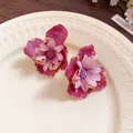 Primer plano de elegantes pendientes de flores magenta con borde dorado en un plato de color crema - Púrpura-Rosa