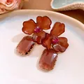 Close-up of acrylic flower earrings featuring a faceted purple gemstone pendant. - Amber