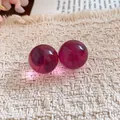 Close-up of translucent dark red resin ball stud earrings on a textured fabric background. - Pink