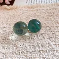 Close-up of translucent green resin ball stud earrings on textured fabric background - Blue