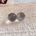 Detail of translucent grey resin ball stud earrings on textured cream fabric - White