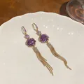 Detailed macro shot of elegant purple rose earrings with long gold tassel chains on a white plate - Hook Style / Gold + Purple