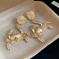 Detailed macro view of golden metallic crab drop earrings with textured square studs - Crab Design / Gold