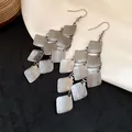 Detail view of matte silver rhombus tassel earrings featuring overlapping metal plates - Black