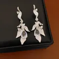 Detailed view of silver teardrop leaf earrings with shimmering zirconia on a black box. - Rose Red / Silver