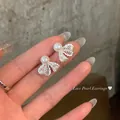 Macro view showing the intricate lace-textured bow earrings with elegant white pearls - Silver