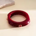 Macro detail of wine red resin bangle with square geometry and crystal embellishments. - Red
