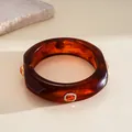 Close-up of a tortoiseshell resin bangle with orange gemstone and rhinestone inlay - Brown