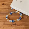 Close-up of colorful flower beaded necklace with stainless steel chain on wooden background. - Bracelet / Blue-Brown