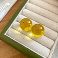 Dettaglio di orecchini a bottone in resina gialla traslucida in un portagioie verde - Sfera / Giallo