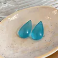 Primo piano dettagliato di orecchini a goccia in resina blu su un piatto di ceramica beige - Blu
