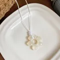 Gros plan d'un pendentif fleur en résine blanc crème sur un collier en cordon blanc - Blanc