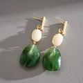Close-up of vintage drop earrings with green and cream resin stones and gold accents. - White-Green