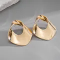 Close-up of artistic gold-tone twisted hollow stud earrings on grey background. - Gold