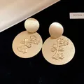 Macro view of golden metal round earrings with textured floral branch relief design - Tops / Gold