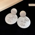Detailed macro view of silver-toned textured round earrings with floral branch pattern. - Tops / Silver