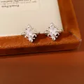 Close-up detail of silver fleur-de-lis cross earrings with central zircon inlay - Silver