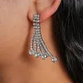 Close-up view of elegant silver rhinestone tassel earrings worn on a model's ear. - Stud Earrings (HE34133) / Silver