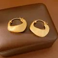 Dettaglio macro di orecchini a cerchio placcati oro 18K con trama spazzolata su scatola marrone - Oro