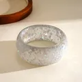 Close-up detail of a clear resin bangle featuring embedded silver stars and snowflake glitter. - Gray
