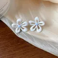 Dettaglio ravvicinato di eleganti orecchini a lobo a fiore in smalto bianco con centro blu - Bianco