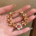 Detailed view of hand wearing a gold-plated bracelet featuring white and pink enamel flower charms - Bracelet / Gold-Pink