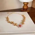Detail showing the intricate red and white enamel flower pendant on a gold necklace. - Necklace / Gold-Red