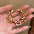 Close-up of elegant gold plated floral bracelet with a white enamel charm on a hand - Bracelet / Gold-Red
