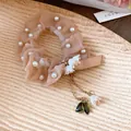 Vista dettagliata di elastico per capelli in organza beige con perle e ciondoli a mughetto. - Marrone