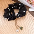 Dettaglio di un elastico in organza nera con perle e ciondoli a foglia dorati - Nero