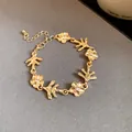 Vista dettagliata di un bracciale dorato con delicati fiori e motivi a ramo elegante. - Bracciale / Oro