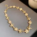 Dettaglio della collana in metallo dorato con motivi floreali irregolari e piccoli cristalli. - Collana / Oro