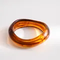Close-up of a vintage amber resin wavy bangle bracelet with a glossy finish. - Amber