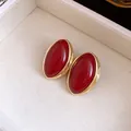 Detalle de elegantes pendientes de resina roja ovalada con borde dorado de estilo vintage - Burdeos