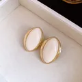 Primer plano de pendientes de resina ovalados vintage con marco de metal dorado brillante - Crema