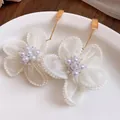 Detailed macro view of white mesh flower earrings with central pearls on a white plate. - White