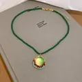 Close-up of vintage necklace featuring dark green beads and a colorful zircon pendant. - Round Base / Green