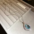 Primer plano del elegante collar con colgante de circón azul en bandeja de joyería gris - Collar Plateado / Azul