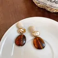 Macro view of vintage Maillard resin earrings with golden accents on a white plate - Gold White and Coffee Patchwork
