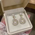 Close-up of elegant gold teardrop hollow earrings with pavé zirconia in a gift box. - Gold